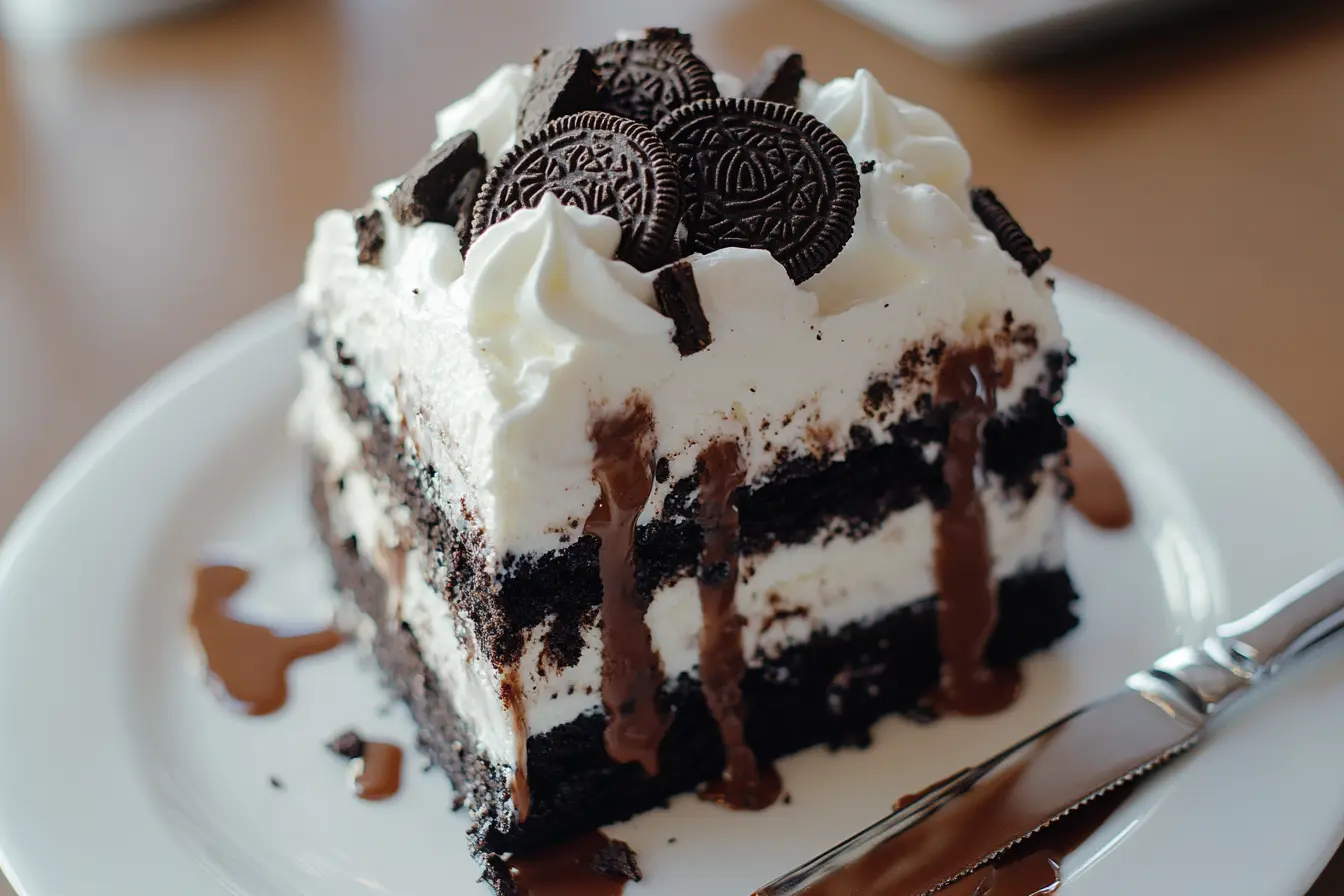 a layered Oreo Blizzard Cake with vanilla soft serve, crushed Oreos, fudge, and whipped cream on a white plate.