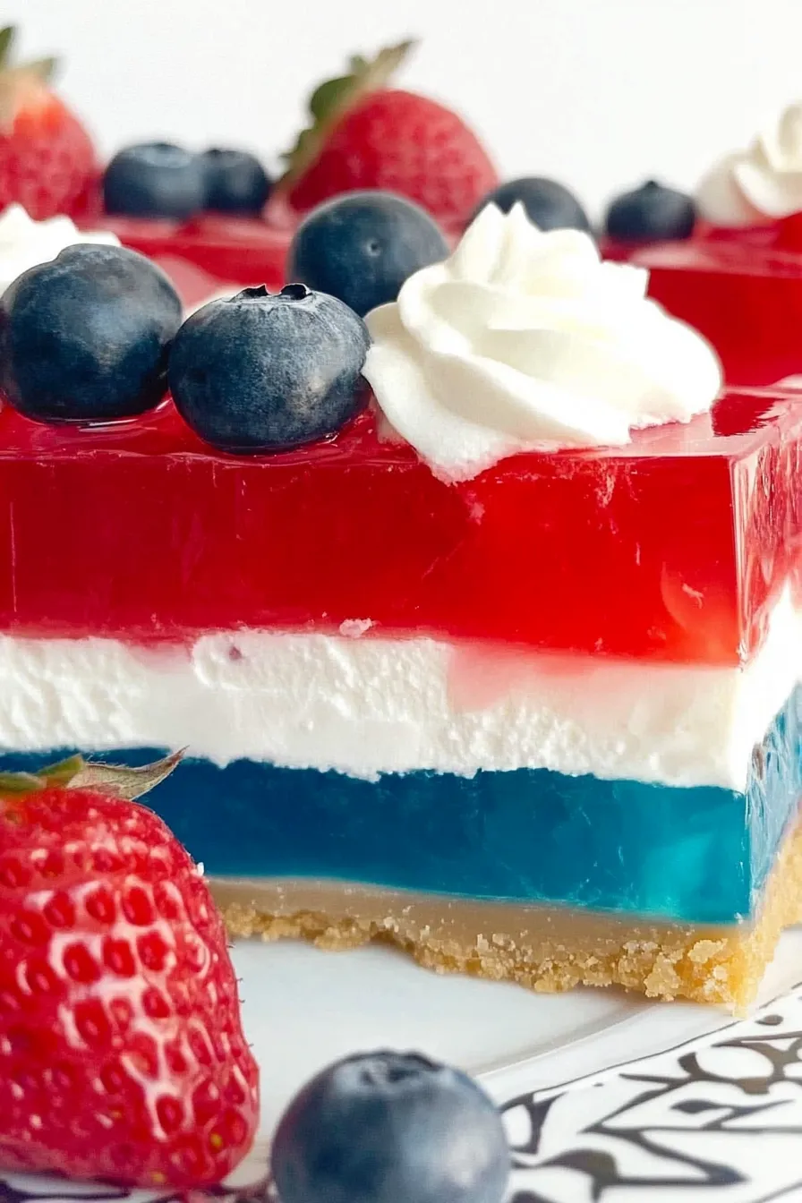 Close-up of 4th of July Patriotic Jello Pie with red, white, and blue layers, whipped cream topping, and fresh berries in a graham cracker crust.
