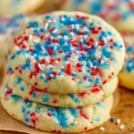 Close-up of chewy 4th of July sprinkle cookies with red, white, and blue sprinkles on a rustic wooden board.