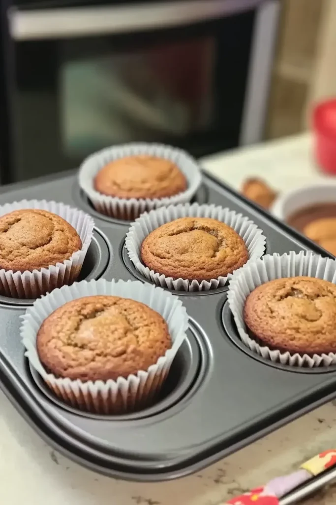 Banana Bread Muffins Recipe: Easy, Moist & Flavorful 7 Freshly baked banana bread muffins in trays, cooling on a kitchen counter with golden tops and clean paper liners.