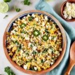 Mexican Street Corn Salad in a rustic bowl with crumbled cheese, cilantro, and lime on a terracotta table