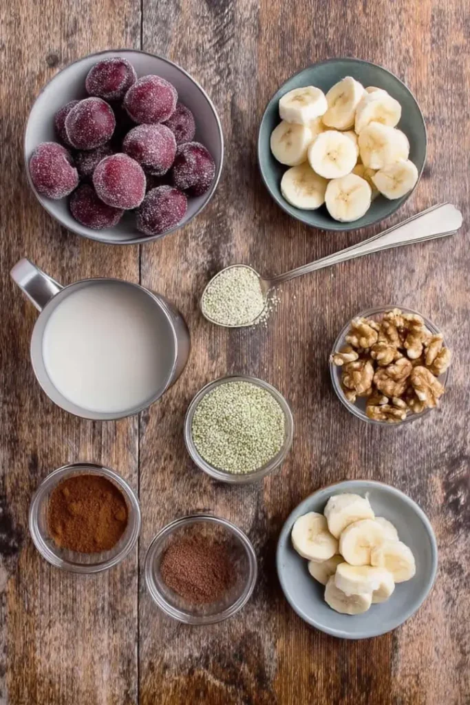 Top-down view of cherry banana smoothie ingredients including frozen cherries, banana slices, almond milk, cinnamon, cloves, walnuts, and hemp seeds.