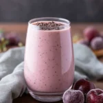 Glass of creamy cherry banana smoothie topped with chocolate chips, surrounded by frozen cherries on a rustic table.