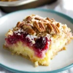 Cherry pineapple dump cake slice with toasted coconut and pecans on a white plate with teal edge, showing gooey cherry filling and golden cake layers.
