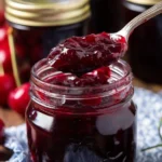 Close-up of homemade cherry vanilla jam in a glass jar with spoon and rustic jar lid