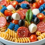 Chilled 4th of July pasta salad with red, white, and blue rotini, pepperoni, black olives, mozzarella, and cherry tomatoes in a white bowl.