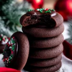 Chocolate Thumbprint Cookies – Rich & Chewy with Ganache Centers 7 Stack of chewy chocolate thumbprint cookies with ganache filling and holiday sprinkles on a festive background.