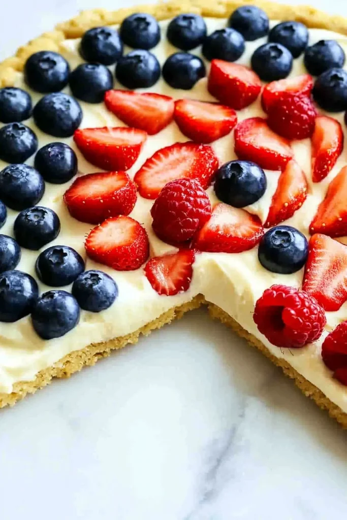 Close-up of 4th of July fruit pizza with sugar cookie crust, cream cheese frosting, and fresh blueberries and strawberries arranged in a festive pattern.