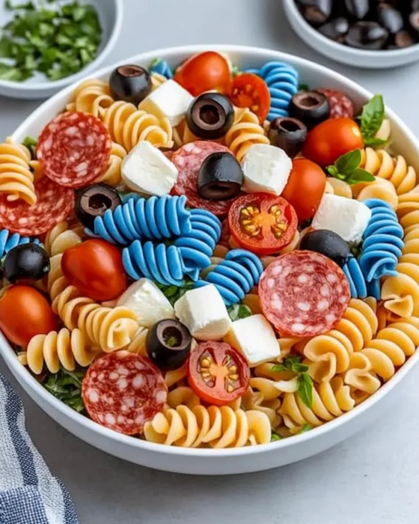 Colorful Chilled 4th of July Pasta Salad with tri-color rotini, pepperoni, mozzarella cubes, and olives in a white bowl, perfect for patriotic celebrations.