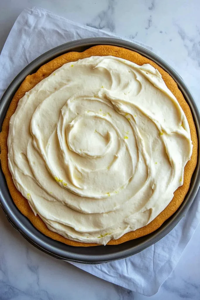 Golden sugar cookie crust topped with swirled cream cheese frosting with lime zest, ready for fruit topping on a 4th of July fruit pizza.