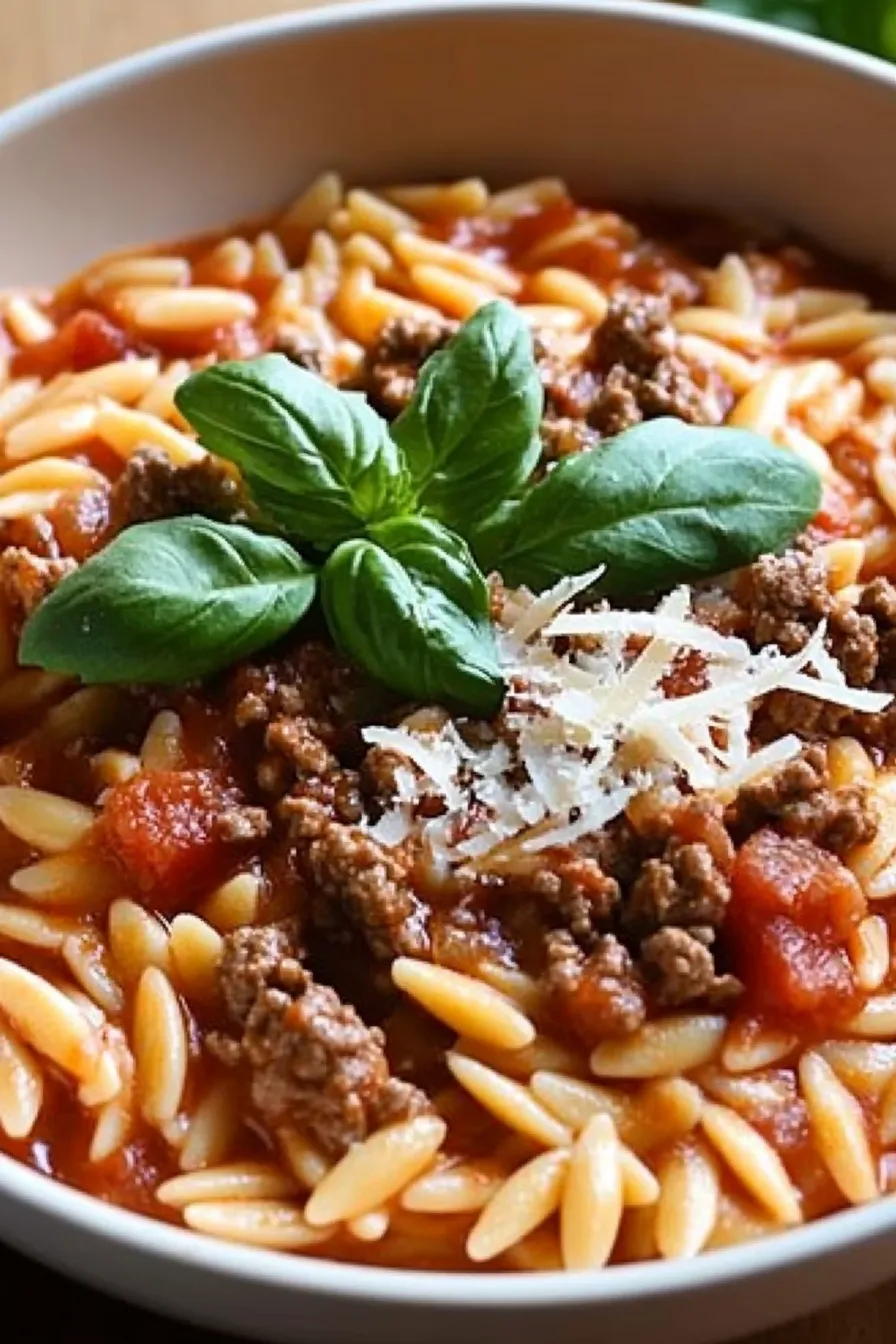 Bowl of creamy tomato ground beef orzo with Parmesan and basil on top in a rich tomato sauce