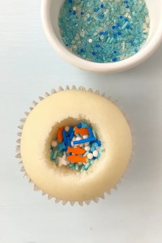 Vanilla cupcake filled with aquatic-themed sprinkles including fish, pearls, and stars.