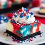 Red White and Blue Cheesecake Bars: Easy Patriotic Dessert for 4th of July 7 Red White and Blue Cheesecake Bar with Oreo crust, topped with whipped cream and patriotic red, white, and blue sprinkles on a white plate