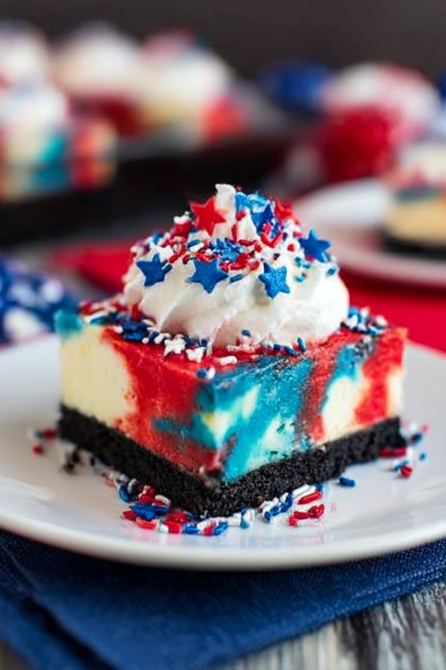 Red White and Blue Cheesecake Bar with Oreo crust, topped with whipped cream and patriotic red, white, and blue sprinkles on a white plate