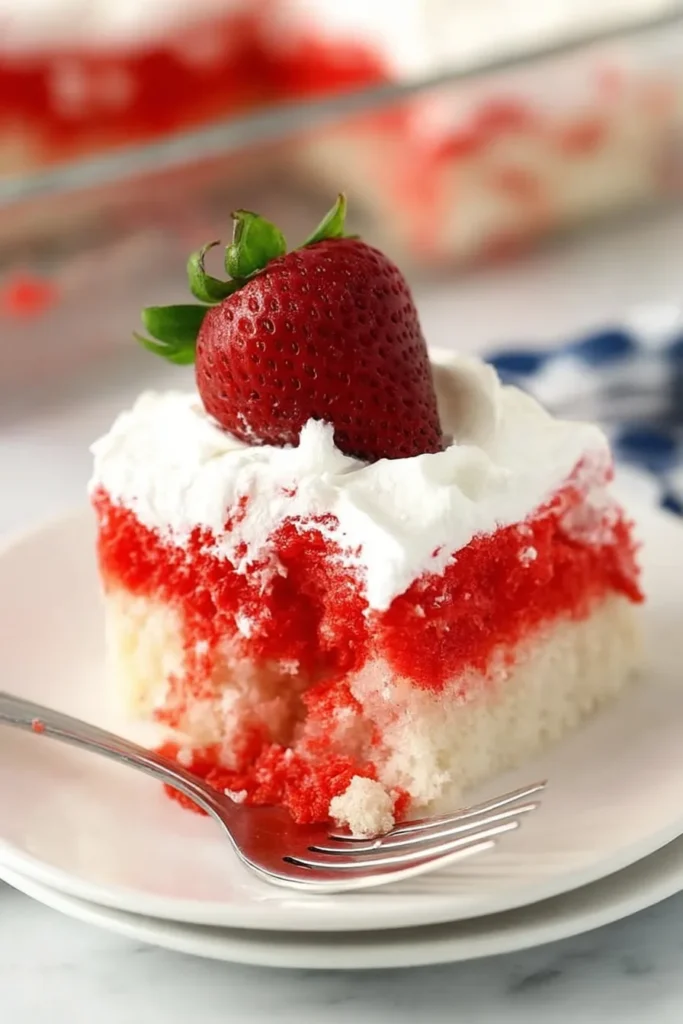 Slice of Strawberry Jello Poke Cake with Cool Whip topping and fresh strawberry on a dessert plate.