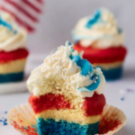 4th of July Cupcakes: Festive, Patriotic, and Simply Delicious! 7 Close-up of a 4th of July cupcake with red, white, and blue layered moist cake topped with swirled white and blue frosting and patriotic star sprinkles on a polished white marble surface.