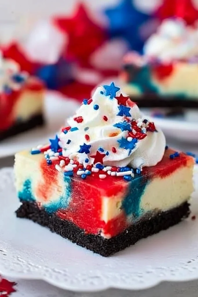 Red White and Blue Cheesecake Bars: Easy Patriotic Dessert for 4th of July 6 Close-up of red, white, and blue swirled cheesecake bar with Oreo crust, whipped cream topping, and patriotic sprinkles on white plate