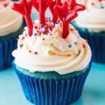 Firecracker Cupcakes – A Festive 4th of July Dessert Idea 7 Festive red, white, and blue firecracker cupcake with white frosting, sprinkles, and licorice on a red cake stand for 4th of July celebrations.