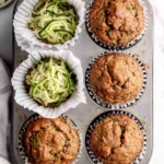 Zucchini Muffins Recipe: Moist, Easy & Perfect for Breakfast 9 Freshly baked zucchini muffins in a muffin tin with grated zucchini on a kitchen counter