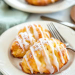 Golden brown peach fritters with powdered sugar glaze on a decorative white plate, showcasing crispy texture and homemade appearance.