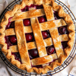 Golden lattice cherry pie with juicy filling on a cooling rack, styled with fresh cherries and vintage pie server.