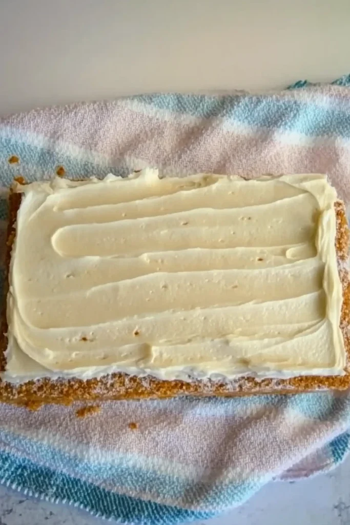 Unrolled carrot cake with cream cheese frosting spread on top, ready to be rolled using a kitchen towel.