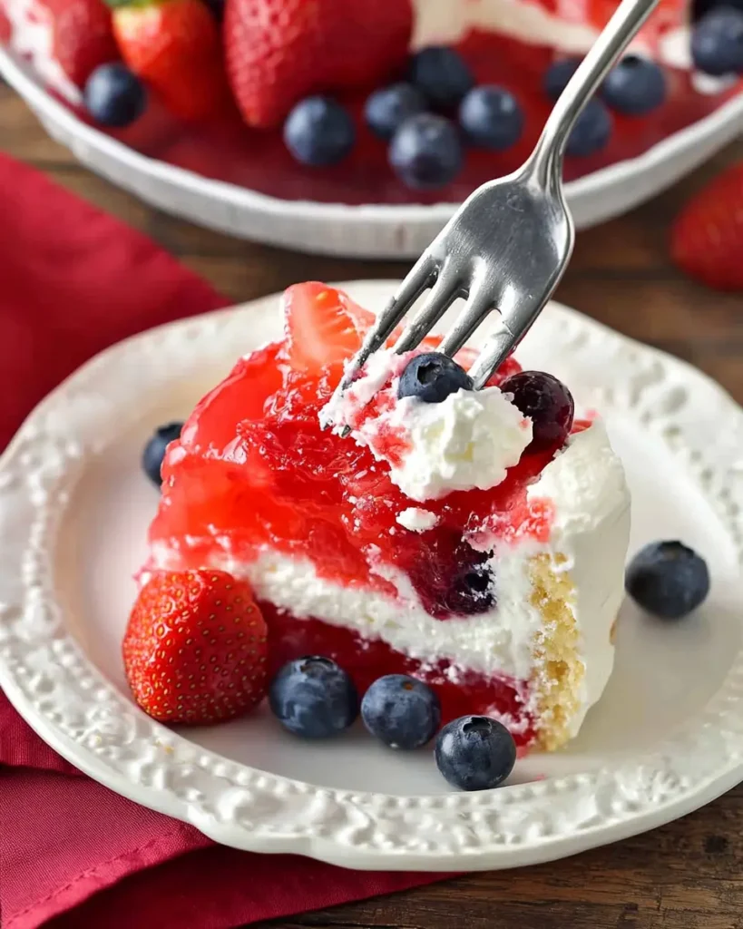 Flag Cake Recipe: Easy Strawberry Jello Dessert for July 4th 8 Close-up of a slice of flag cake with whipped cream, strawberries, blueberries, and Jello-soaked white cake layers.