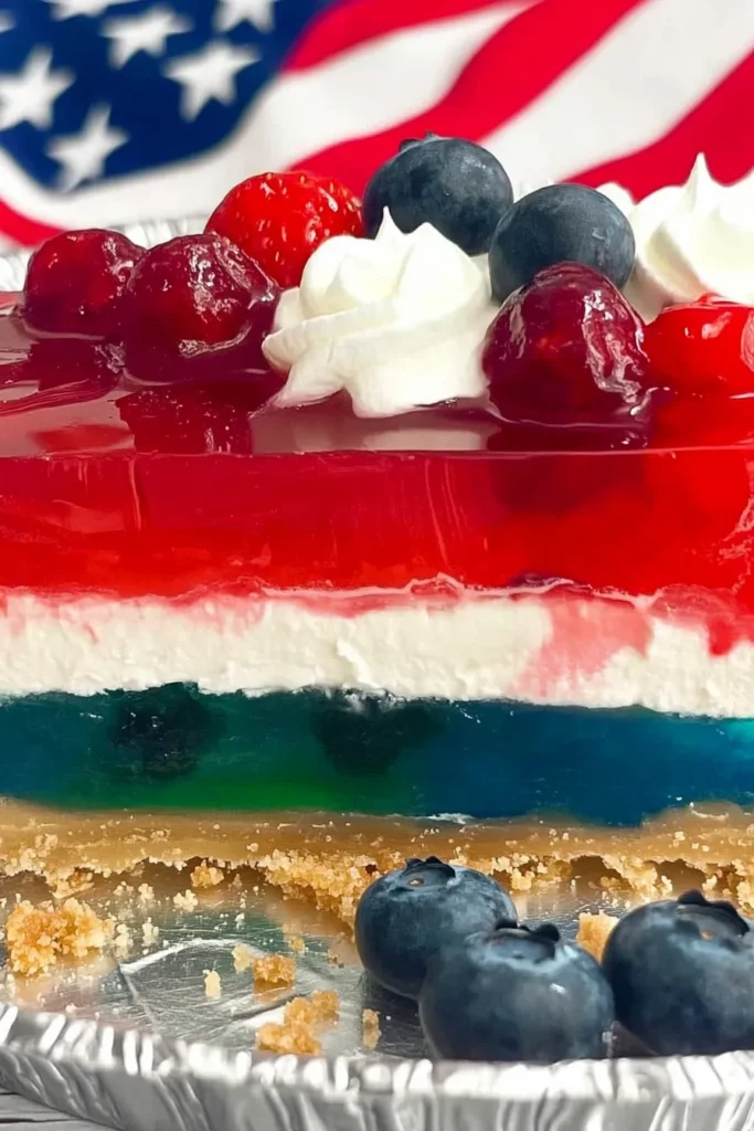 4th of July Patriotic Jello Pie: A No-Bake Red, White & Blue Treat 8 Partially sliced 4th of July Patriotic Jello Pie with red, white, and blue layers, topped with whipped cream and berries in a foil pie dish.