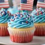 Patriotic Bomb Pop cupcakes with swirled blue frosting, festive sprinkles, and mini American flags, styled on a white stand.