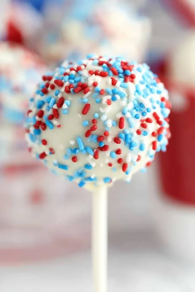 Decorated 4th of July cake pop covered in white chocolate and patriotic sprinkles.