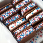 Patriotic mini ice cream sandwiches coated in red, white, and blue star-shaped sprinkles in a metal tray lined with parchment paper.