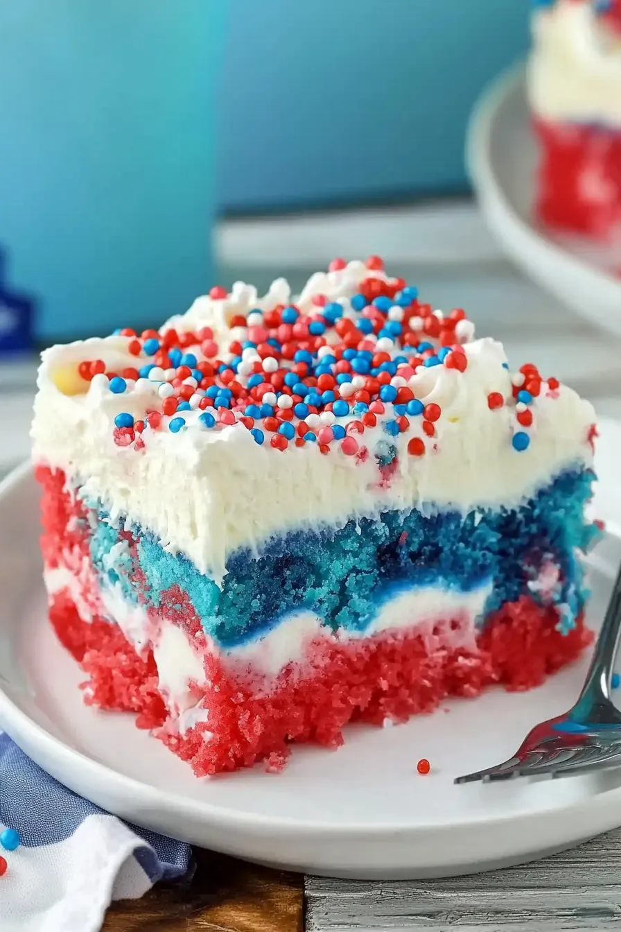Slice of Patriotic Poke Cake with red, white, and blue layers, topped with whipped cream and sprinkles on a plate.