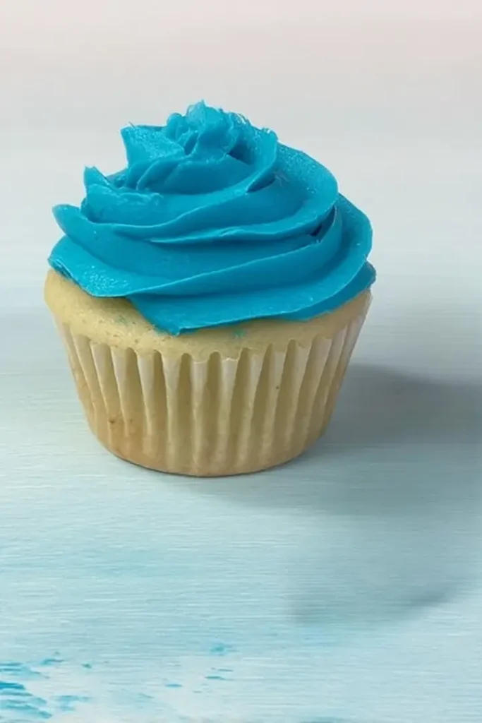 Vanilla cupcake with blue frosting swirl beside piping bag with star tip.