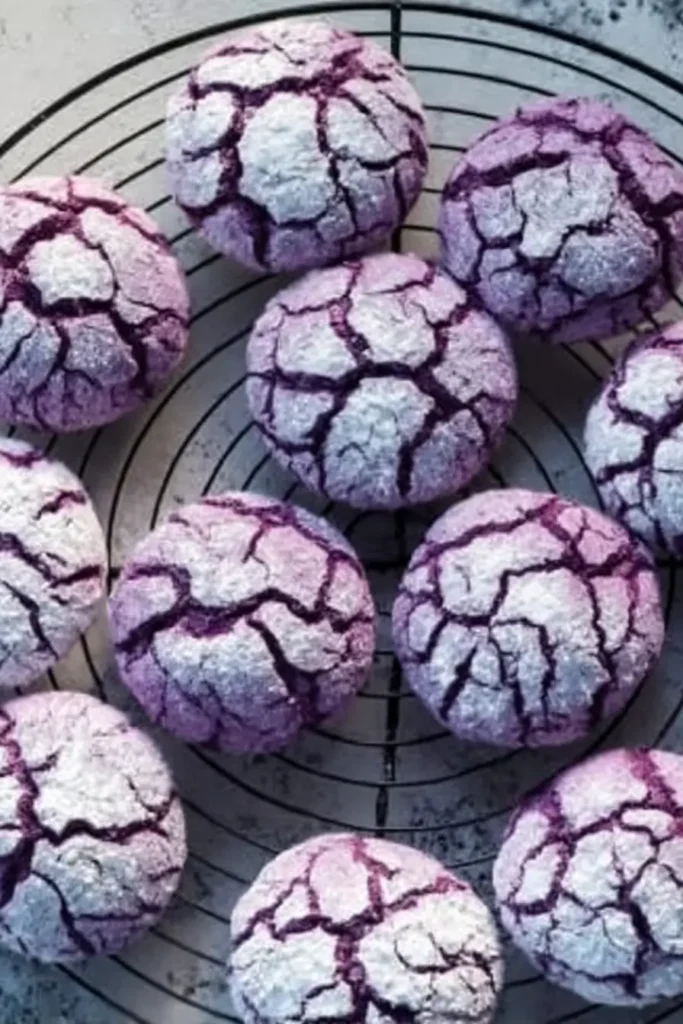 A batch of purple crinkle cookies with powdered sugar tops cooling on a wire rack.