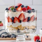 Red, white, and blue trifle dessert in a glass bowl with layers of whipped cream, pudding, strawberries, and blueberries, festive 4th of July treat.