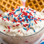 Red White and Blue Funfetti Dip – Easy No-Bake Party Treat 15 Red, White and Blue Funfetti Dip in a bowl topped with patriotic sprinkles and waffle cookies, surrounded by festive dippers.