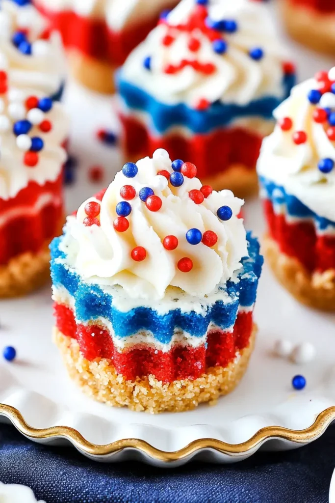 Red White and Blue Mini Cheesecakes – A Patriotic Dessert to Savor! 5 festive Red, White, and Blue Mini Cheesecakes topped with whipped cream and sprinkles, arranged on a rustic ceramic tray.