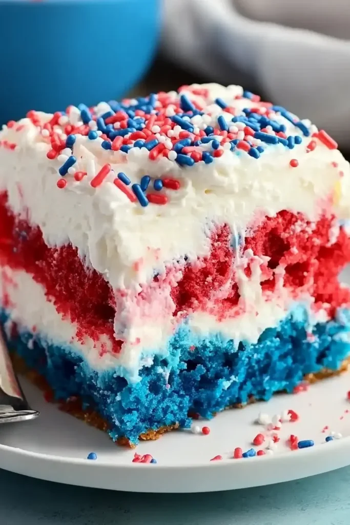 Patriotic Poke Cake: The Ultimate 4th of July Dessert 12 Slice of Patriotic Poke Cake with whipped topping, sprinkles, and bite taken out