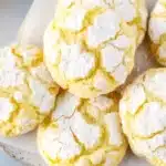 Lemon Crinkle Cookies: A Soft, Citrus Hug in Every Bite 9 Soft lemon crinkle cookies coated in powdered sugar on a blue rustic surface with bright citrus tones