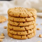 Peanut Butter Cookies Recipe: Easy, Soft & Chewy Classic Treats 7 Stack of golden-brown classic peanut butter cookies with fork marks, sprinkled with sea salt and peanuts, on a smooth beige marble surface with cream linen background.