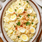 Creamy Southern potato salad garnished with paprika, parsley, and sliced hard-boiled eggs in a serving dish.