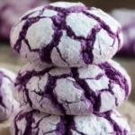 Stack of three cookies from a Purple Crinkle Cookies Recipe with cracked powdered sugar tops, resting on parchment paper.