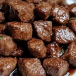 Juicy and tender cubed steak bites with a glossy brown sauce, served on a white plate with a neutral background.