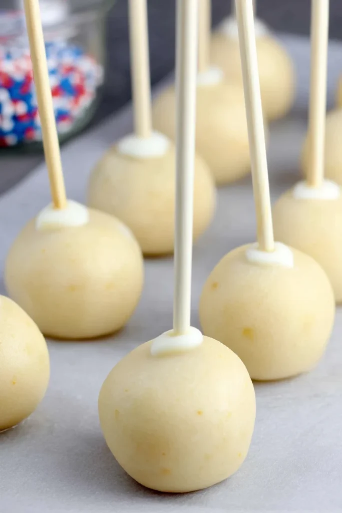Uncoated vanilla cake pops with sticks inserted, ready for chilling on parchment paper.