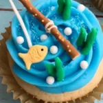Gone Fishing Cupcakes decorated with blue frosting, pretzel stick fishing poles, goldfish crackers, fondant greenery, and sugar pearl bubbles.