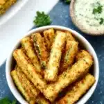 Air Fryer Zucchini Fries: Crispy, Cheesy & Guilt-Free 7 Golden crispy air fryer zucchini fries in a white bowl with dipping sauce and parsley on a speckled background.
