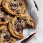 Soft banana bread chocolate chip cookies with melty chocolate chips and sea salt in a rustic tray, one cookie with a bite taken out