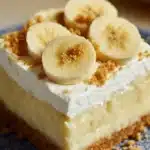Banana Pudding Cheesecake Bars: Easy & Creamy Dessert Recipe 7 Close-up of a banana pudding cheesecake bar with whipped cream, banana slices, and graham cracker crust on a plate.