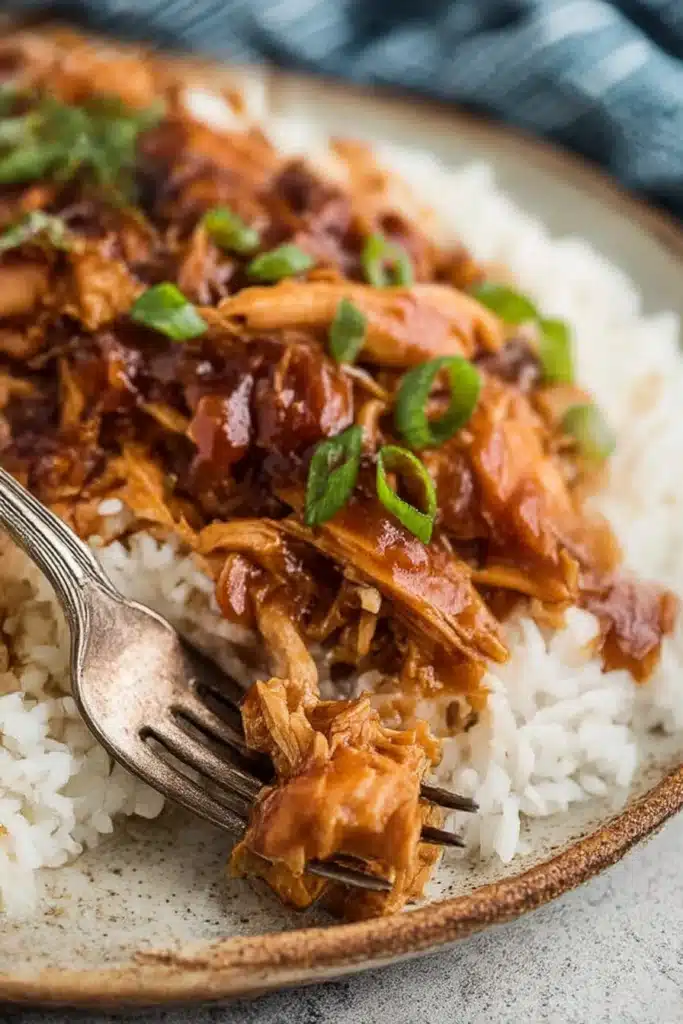Crock Pot Bourbon Chicken – Sweet, Sticky & Comforting Slow Cooker Classic 8 Bourbon chicken over white rice on a ceramic plate with a fork, coated in sticky sauce and garnished with green onions.