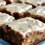 Moist banana bread brownies topped with brown butter frosting on a ceramic plate